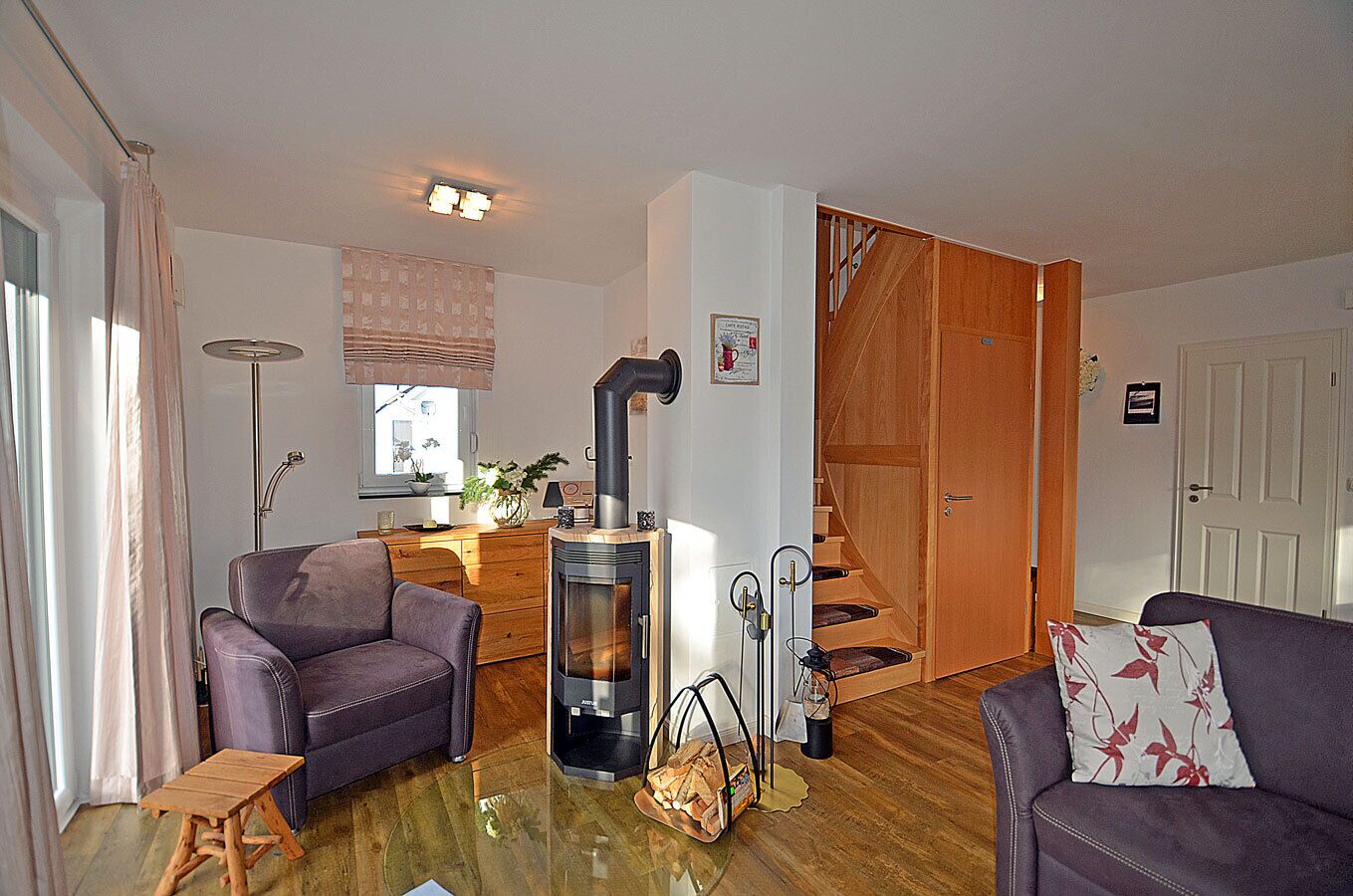A living room with a sofa, a chair, a small table, a fireplace, and a staircase leading to another room.