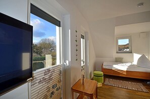 Ein Schlafzimmer mit einem Bett, einem Fenster, einem kleinen Tisch und einer grünen Mülltonne.