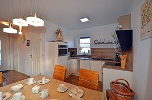 A modern kitchen with white cabinetry, a dining table set with cups and plates, and a television mounted on the wall. - High-quality, tastefully furnished with a fireplace, sleeps up to 4, Wi-Fi, washing machine (Breege)