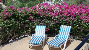 Two sun loungers with striped cushions, positioned on a sandy surface, with a backdrop of blooming pink bougainvillea. - Villa Tavla (KAŞ)