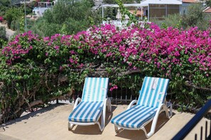 Two sun loungers with striped cushions, positioned on a sandy surface, with a backdrop of blooming pink bougainvillea. - Villa Tavla (KAŞ)