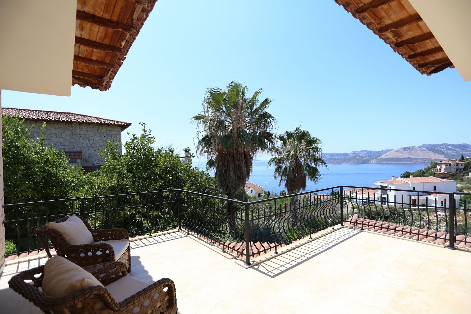 Un balcone con mobili in vimini, un edificio in pietra e vista sul mare e sulle montagne.
