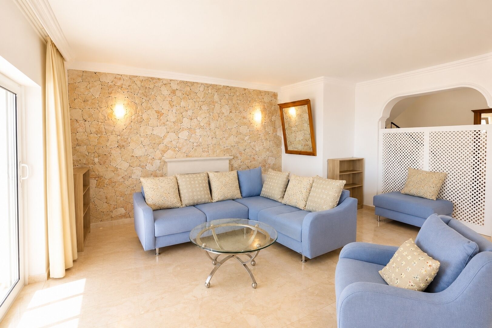 Una sala de estar con una pared de piedra, un sofá azul, una mesa de centro de vidrio y una consola blanca.