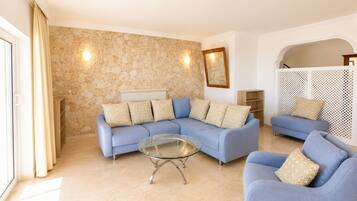 Una sala de estar con una pared de piedra, un sofá azul, una mesa de centro de vidrio y una consola blanca.