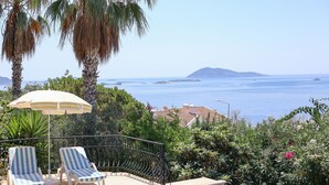 A poolside area with two lounge chairs, an umbrella, and a view of the sea. - Villa Tavla (KAŞ)