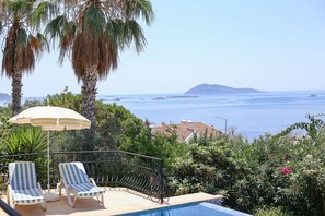 A poolside area with two lounge chairs, an umbrella, and a view of the sea. - Villa Tavla (KAŞ)