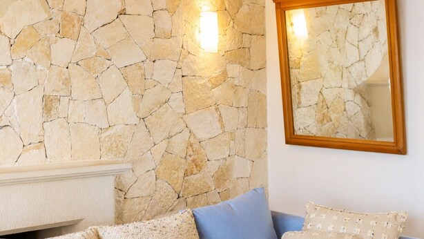 A room with a stone wall, a wooden-framed mirror, and a blue sofa with patterned cushions. - Villa Tavla (KAŞ)