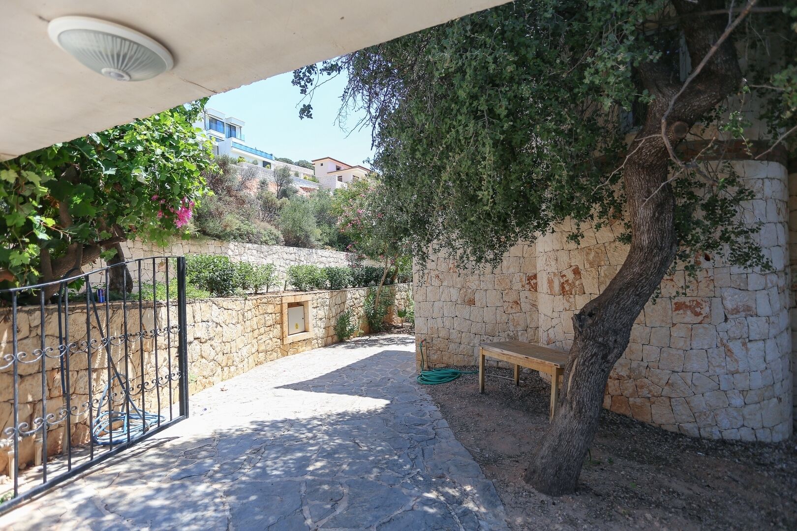 A stone-walled outdoor area with a bench, a tree, and a metal gate.