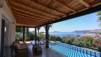 Un espacio al aire libre techado con piscina, mobiliario y vistas al mar.