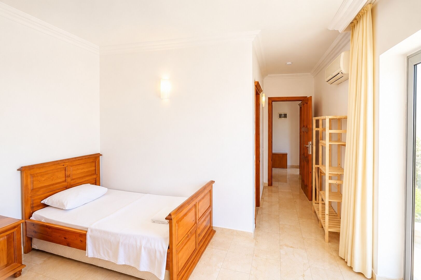 Ein Schlafzimmer mit einem hölzernen Bett, einem Nachttisch, einem Kleiderschrank und einem durch eine offene Tür einsehbaren Badezimmer.