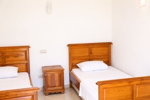 A room with two wooden beds, a small wooden nightstand, and a white wall. - Villa Tavla (KAŞ)