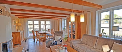 A spacious living area with a wooden ceiling, a fireplace, a sofa, a coffee table, and a dining area with chairs and a table.