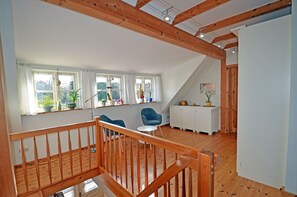 A room with a wooden staircase, a dining area with a table and chairs, and a kitchen area with cabinets and a countertop.