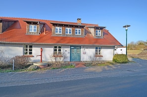 En tvåvåningsbyggnad med ett rött tegeltak, en ytterdörr och en liten trädgårdsyta.