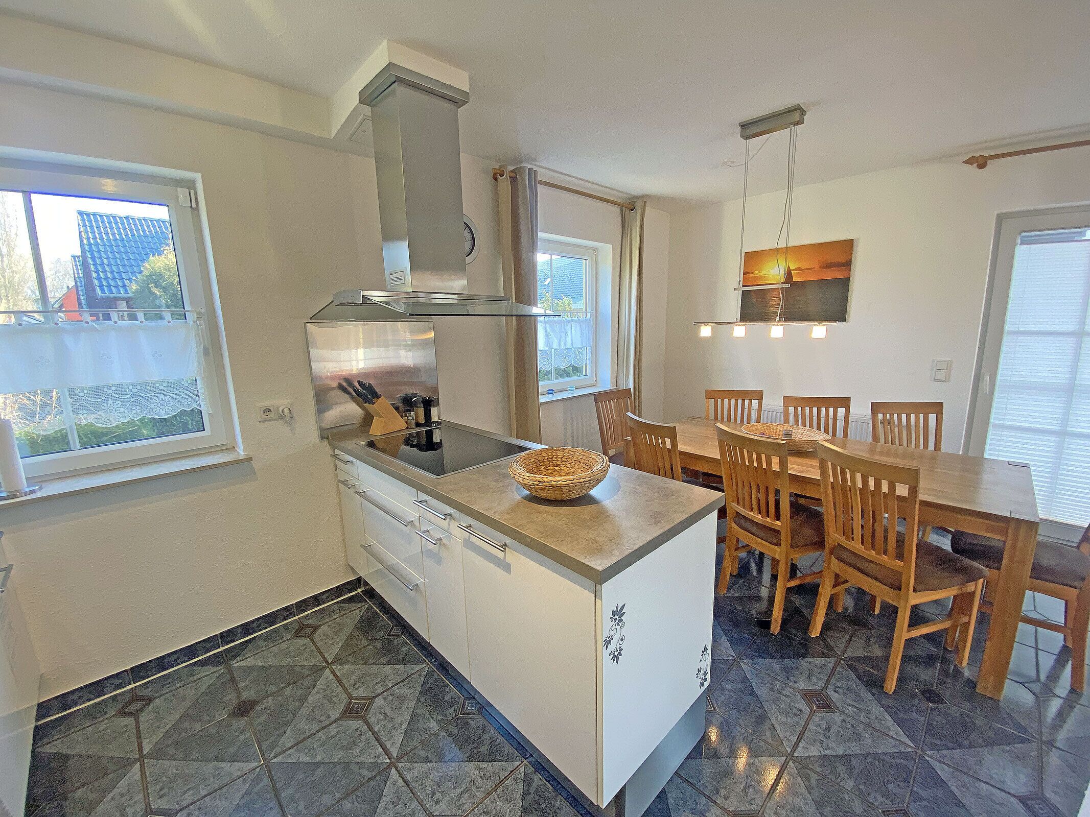 Una cocina con una isla central, mesa de comedor, sillas y vistas al exterior.