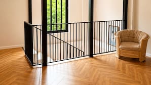 A spacious room with a wooden herringbone floor, a black metal railing, and a wicker chair. - The Green O (Oni)