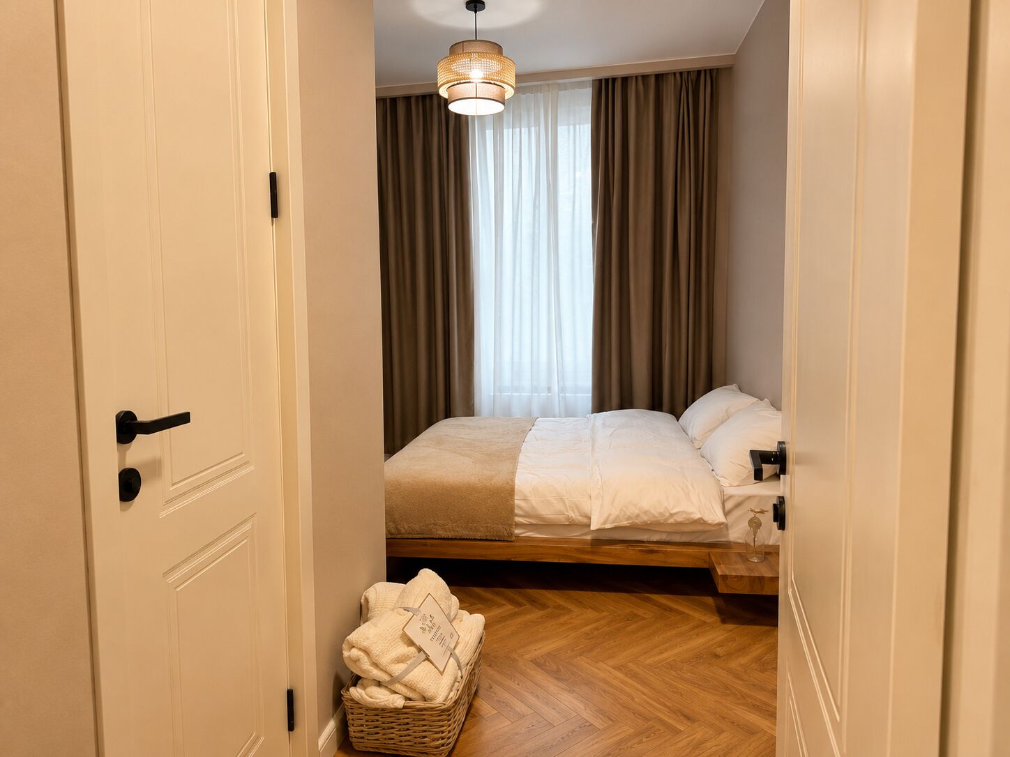 A hotel room with a bed, a bedside table, a hanging light fixture, and a window with curtains.