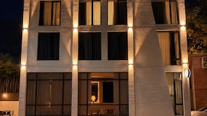 A multi-story building with large windows and a flat roof, featuring a well-lit entrance and a visible outdoor seating area. - The Green O (Oni)