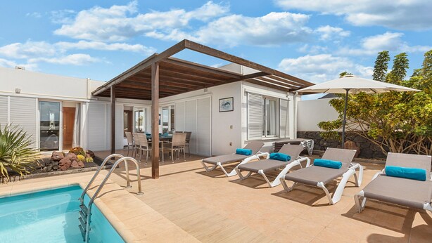 Et poolområde med liggestole, en overdækket terrasse og en pool.
