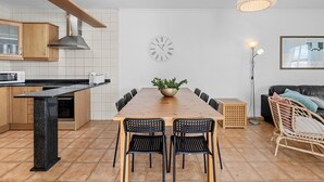 Et moderne køkken med en træø, et spiseområde med et træbord og stole, et vægur og en gulvlampe.