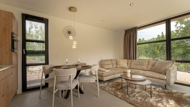 Een moderne woonkamer met een eethoek, grote ramen en uitzicht op groen.