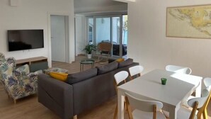 A modern living room with a sofa, a TV, and a dining table with chairs. - Apartments Vala (Grebaštica)