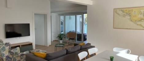 A modern living room with a sofa, a TV, and a dining table with chairs.