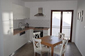 A compact kitchen with white cabinets, a gas stove, a sink, and a dining area with a wooden table and white chairs.