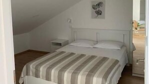 A bedroom with a sloped ceiling, a bed with a striped bedspread, a bedside table, and a wall-mounted light fixture. - Apartments Vala (Grebaštica)