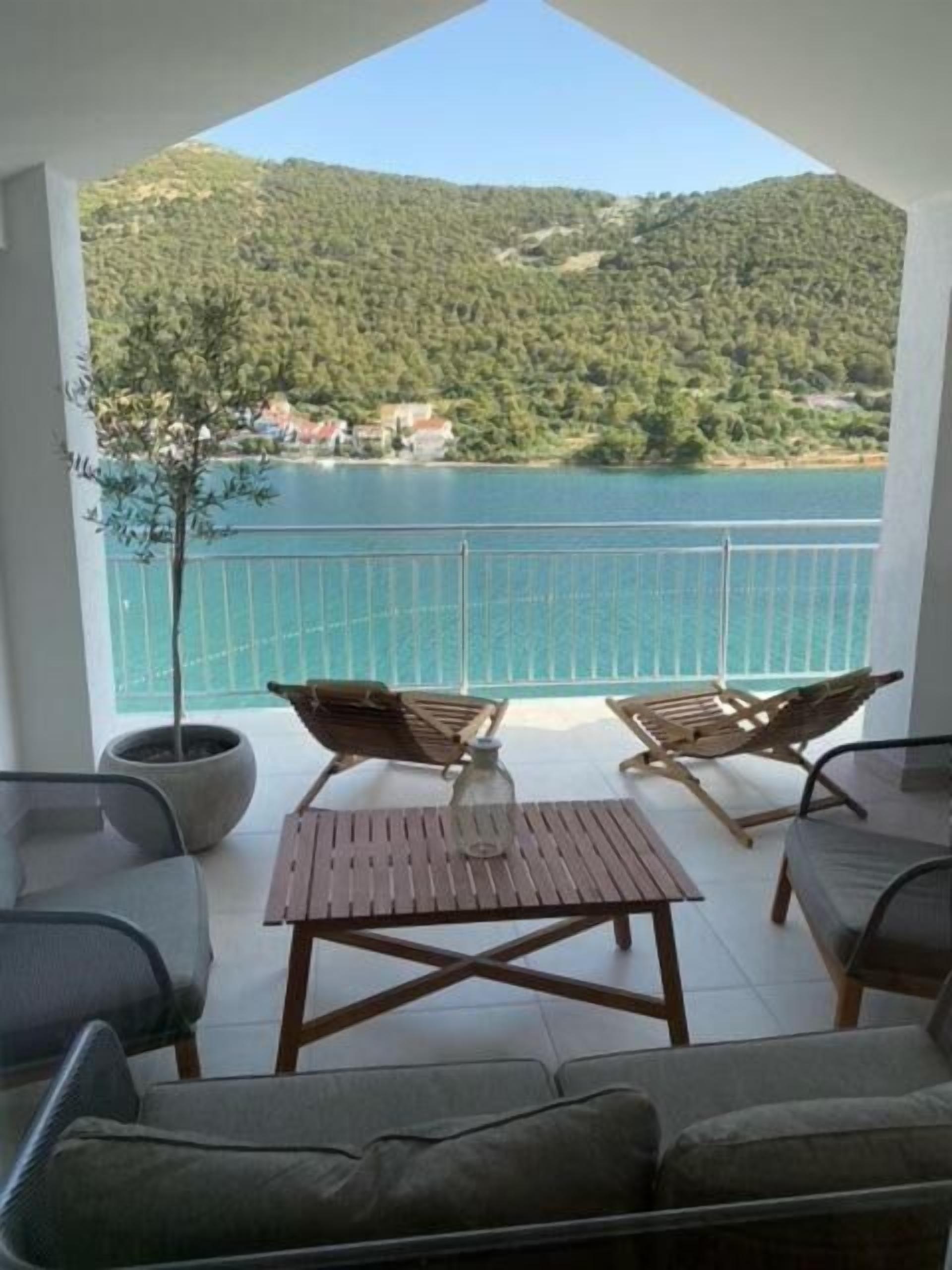 A balcony with a view of a lake and hills, furnished with a sofa, two chairs, and a table.