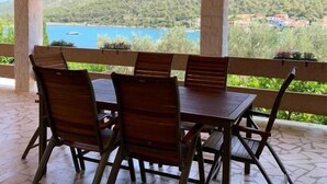 An outdoor covered patio with a table and chairs, overlooking a scenic view of a body of water and greenery. - Apartments Vala (Grebaštica)