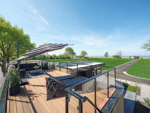 Eine moderne Außenterrasse mit Glasgeländer, Holzbelag und Meerblick.