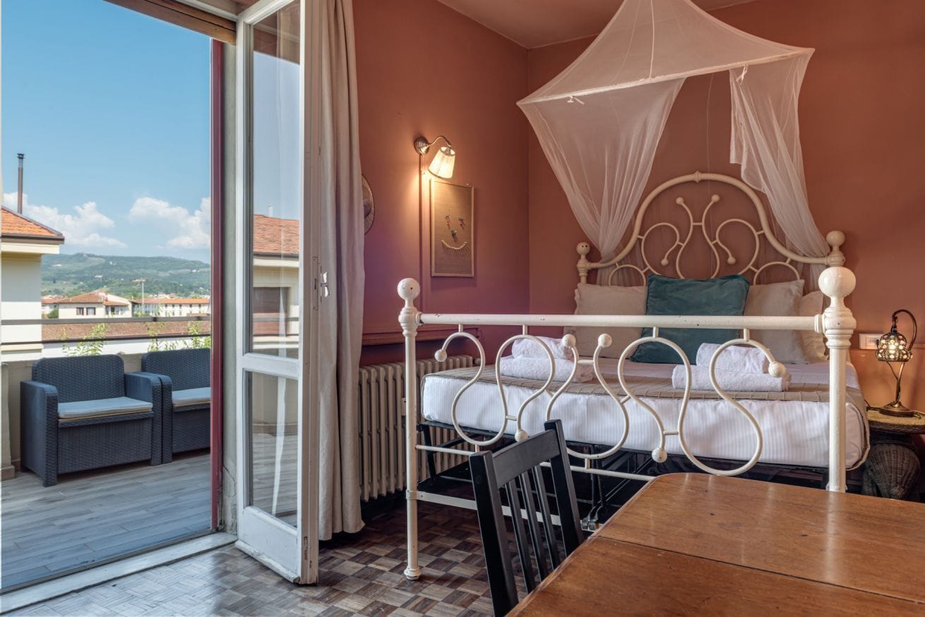 Ein Schlafzimmer mit Bett, Tisch, Stuhl, Nachttischlampe und Blick ins Freie.