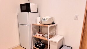 A compact kitchenette with a white refrigerator, microwave, and coffee maker on a shelf, a small trash bin, and a wooden floor. - About a 10-minute walk from Okayama Station / Accommodates up to 6 guests / 1 private parking space available / 3 bedrooms (Okayama City)