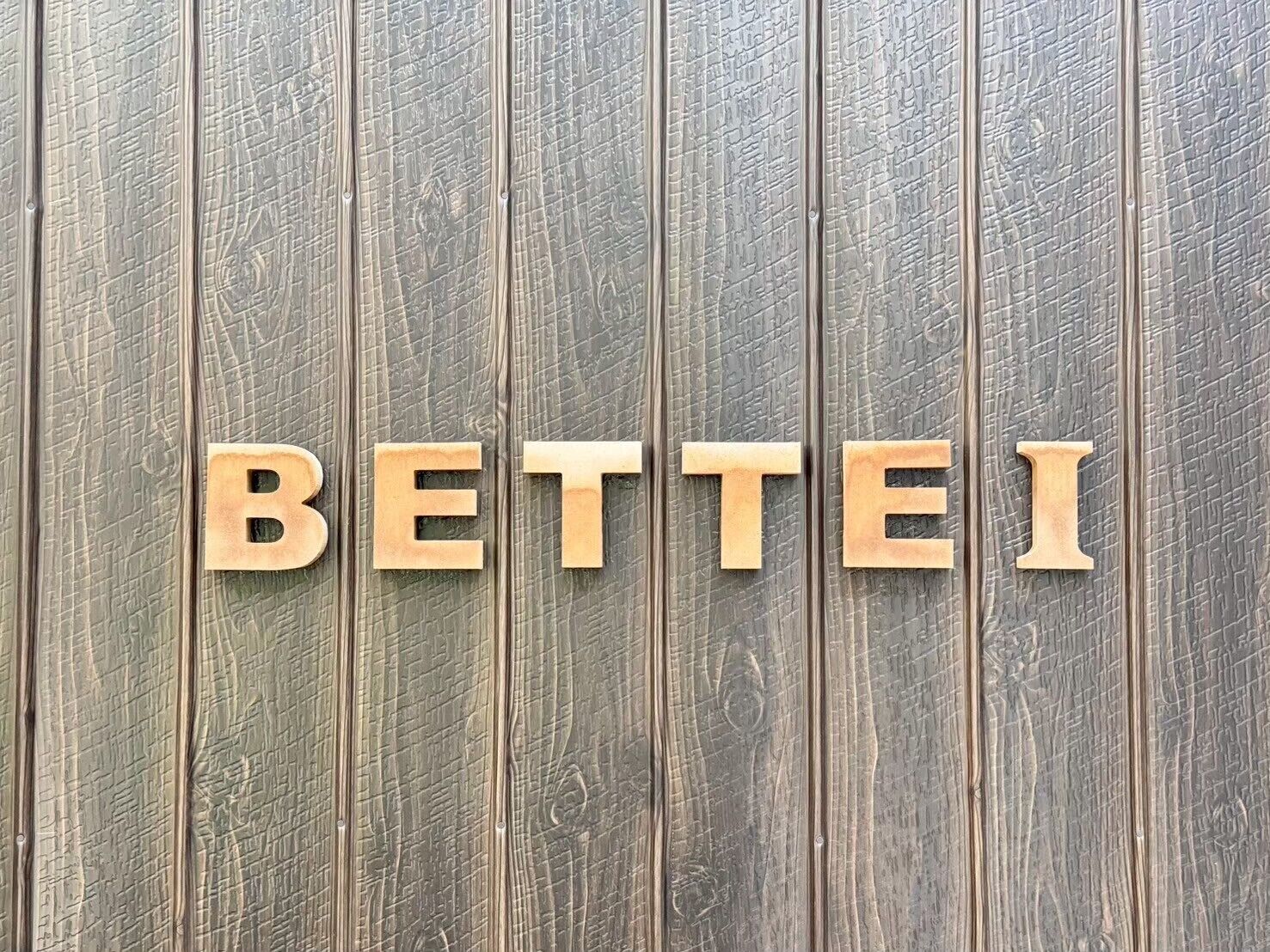 Wooden letters spelling 'BETTEI' on a textured wooden background.