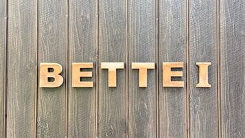 Wooden letters spelling 'BETTEI' on a textured wooden background.