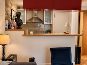 Kompakti oleskelutila, jossa on pieni keittiönurkkaus, patsas, lamppu ja tuoli.