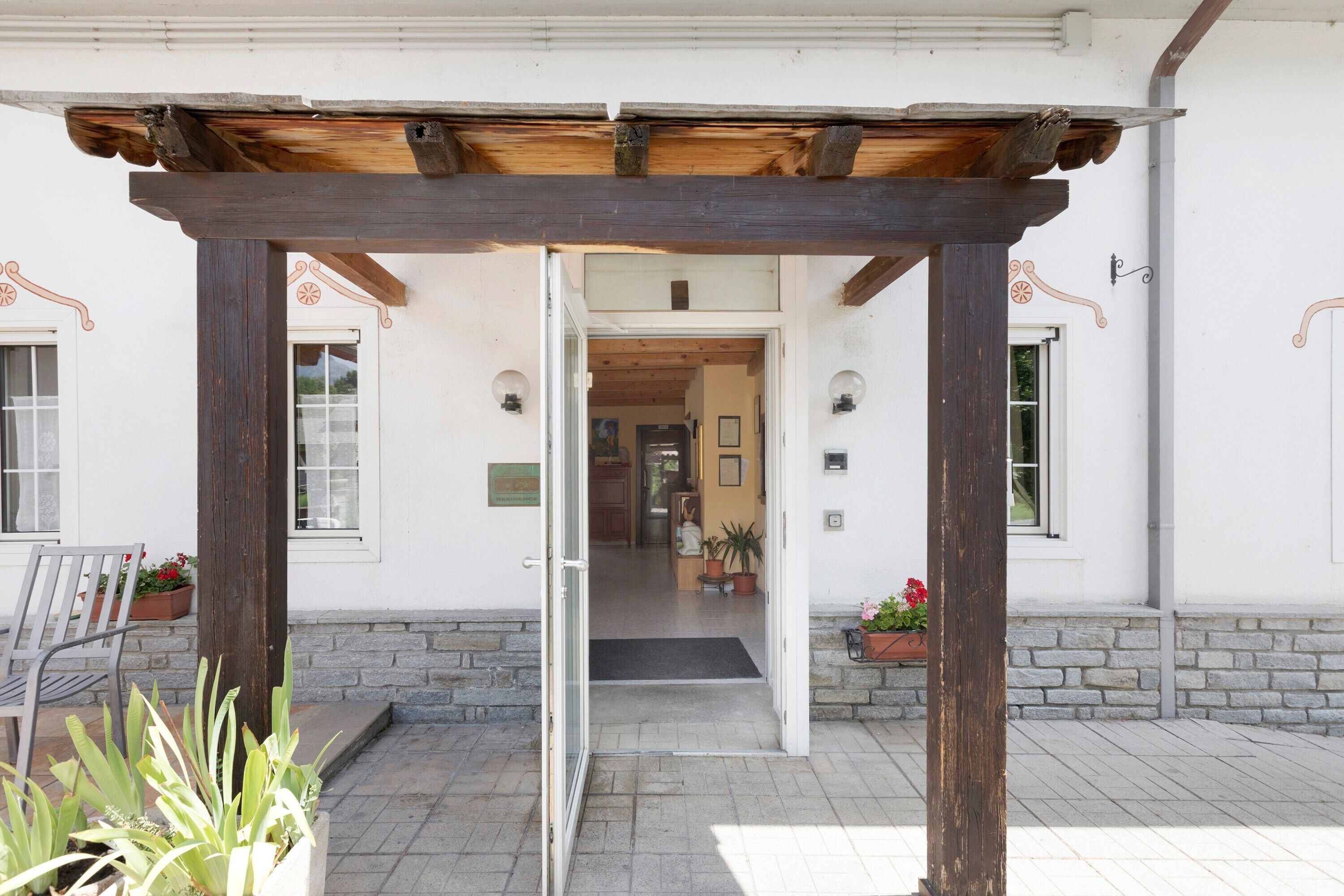 Entrada de edificio con una pérgola de madera, un banco y plantas en macetas.