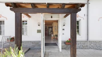 Entrada de edificio con una pérgola de madera, un banco y plantas en macetas.