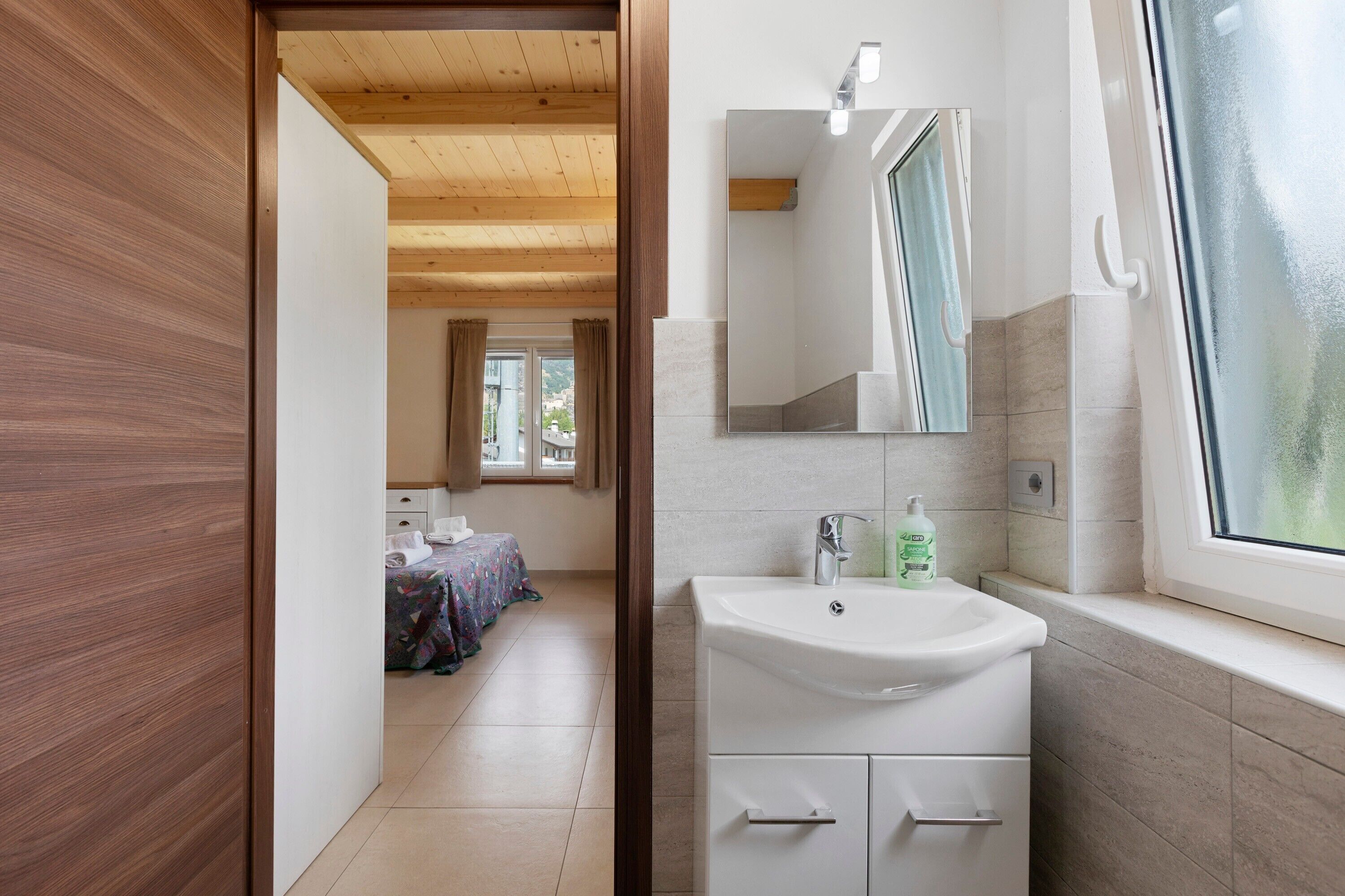 Een moderne badkamer met een witte wasbak, een spiegel en een raam.