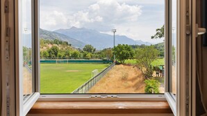 A window view of a green field with a goalpost, a fence, and mountains in the background.