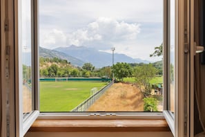 A window view of a green field with a goalpost, a fence, and mountains in the background.
