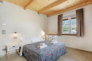 Un dormitorio con cama, mesita de noche, cómoda, ventana con cortinas y vistas al exterior.