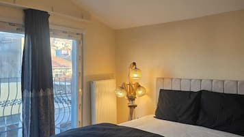 A hotel room with a bed, a window with curtains, a radiator, and a hanging light fixture.