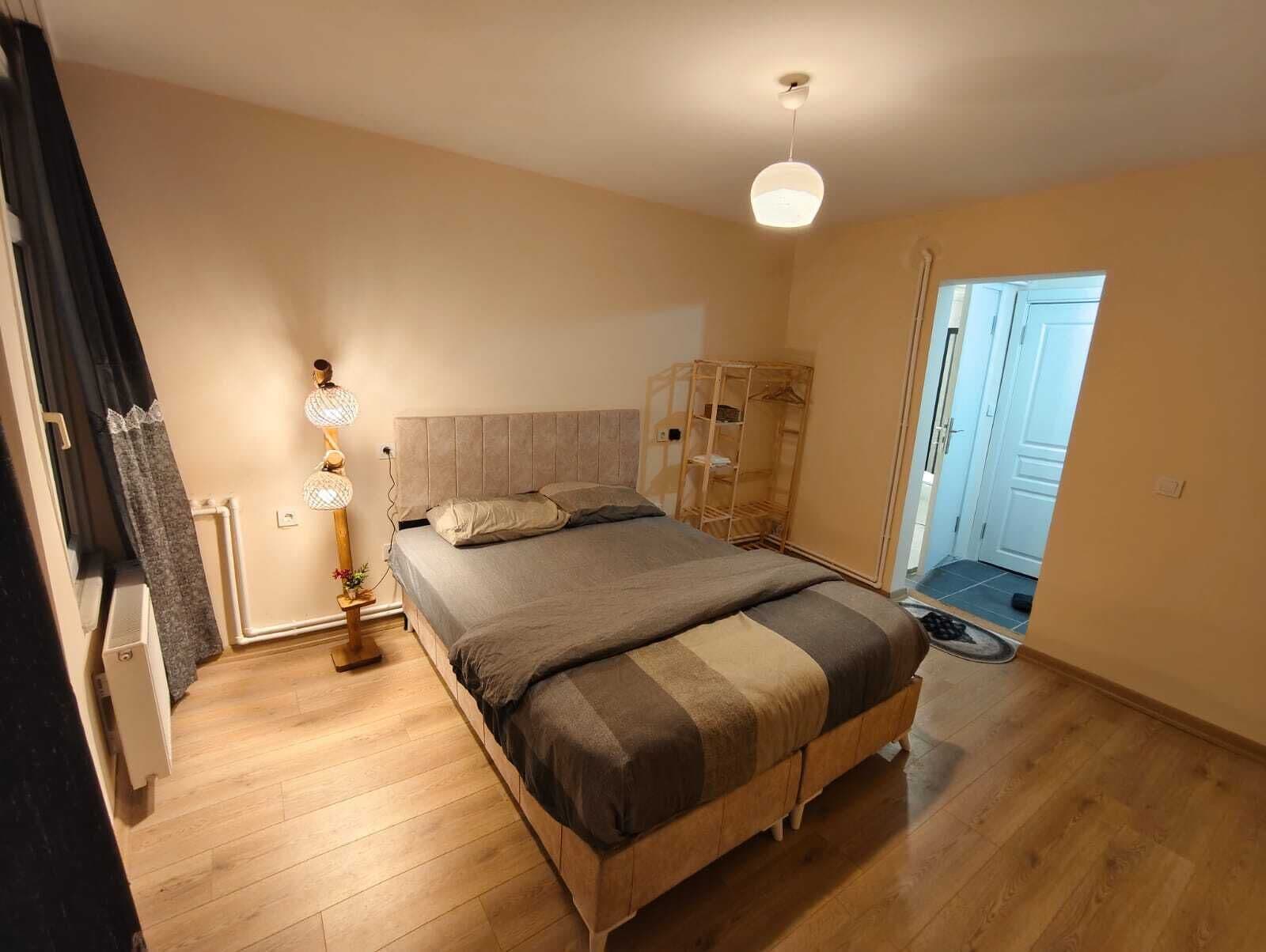 A bedroom with a bed, bedside lamp, wooden wardrobe, and a door leading to another room.
