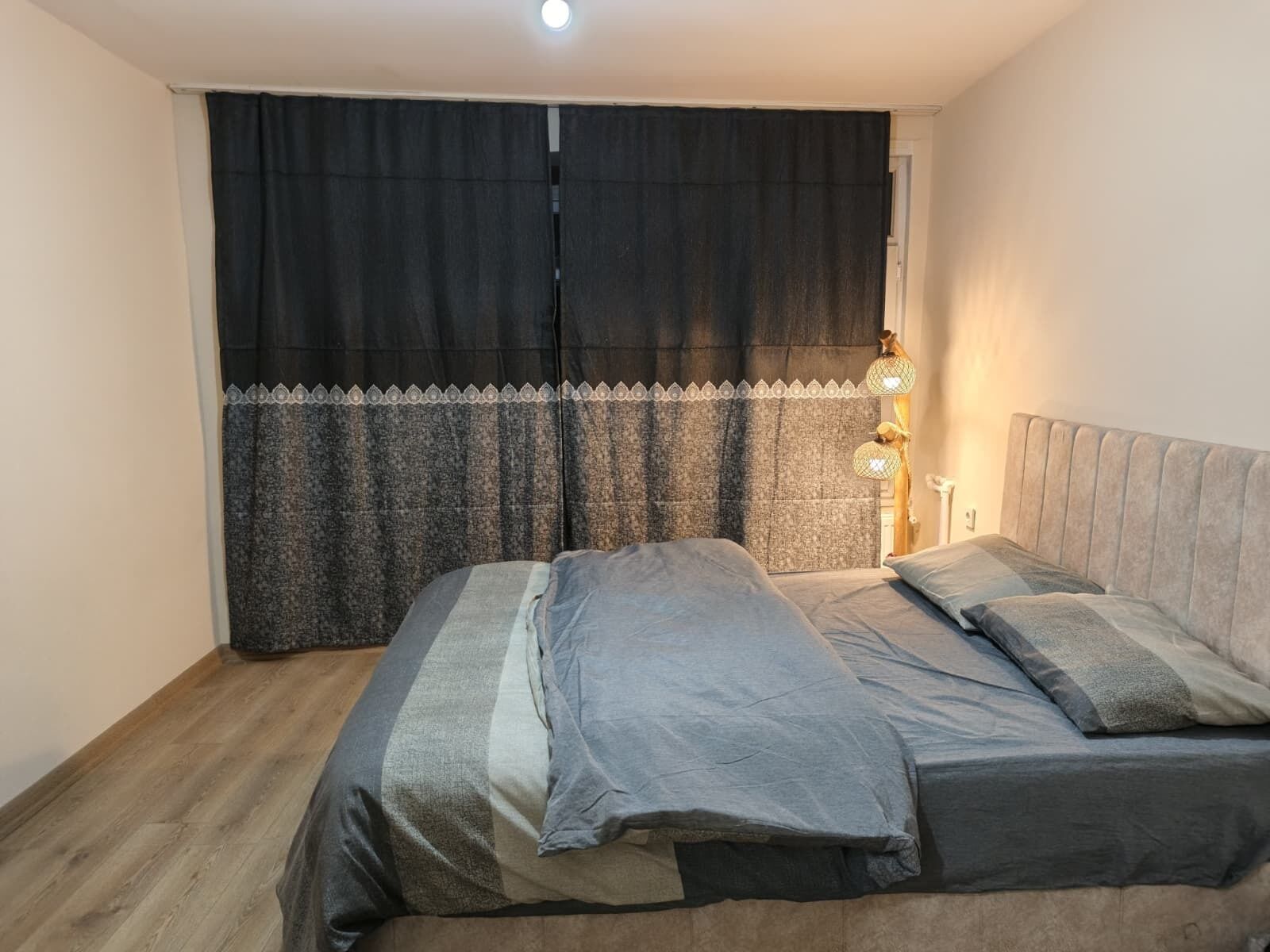 A bedroom with a bed, curtains, and a nightstand with a lamp.