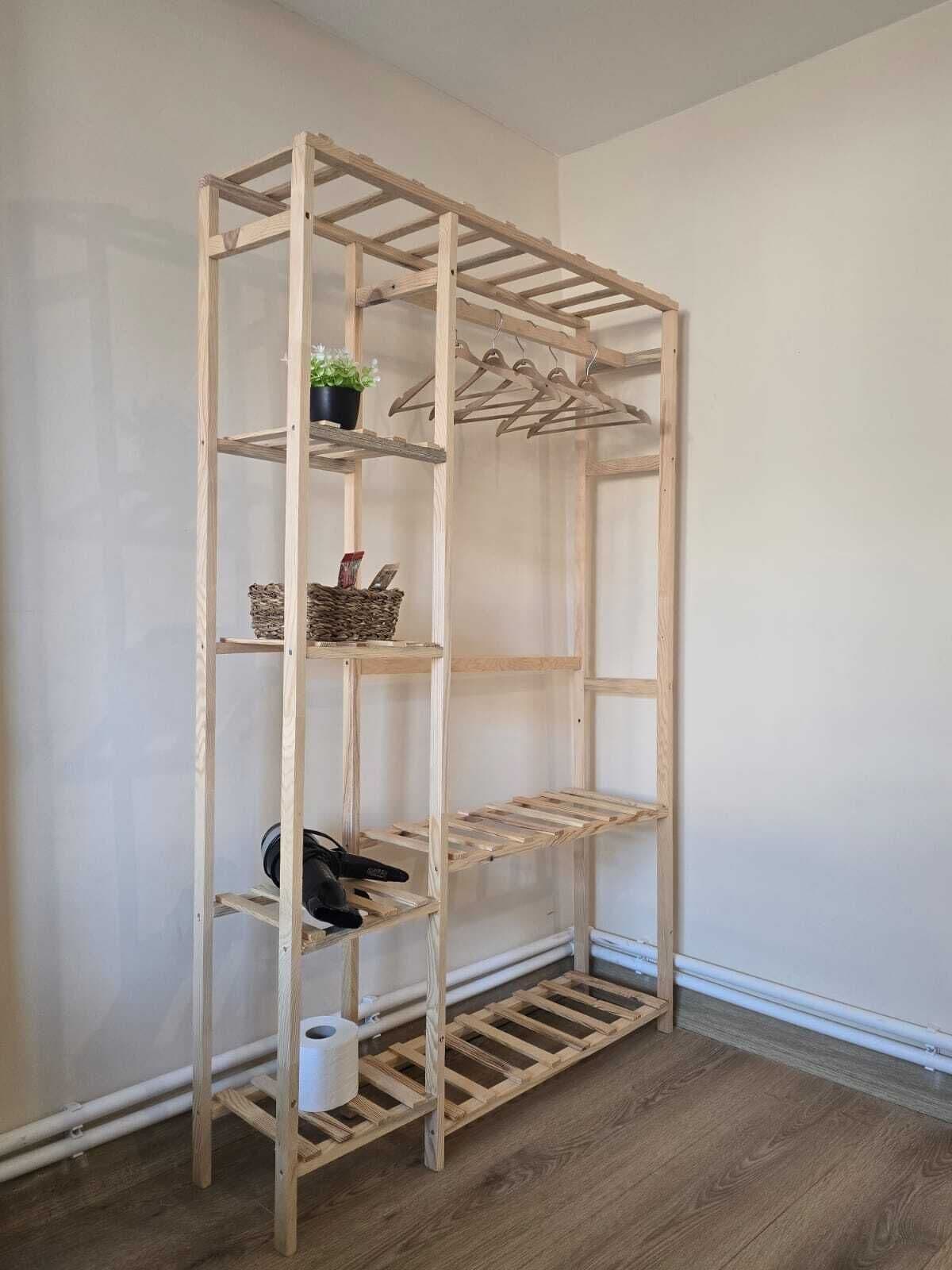 A wooden shelving unit with multiple shelves and a hanging rack, positioned against a plain wall with a wooden floor.