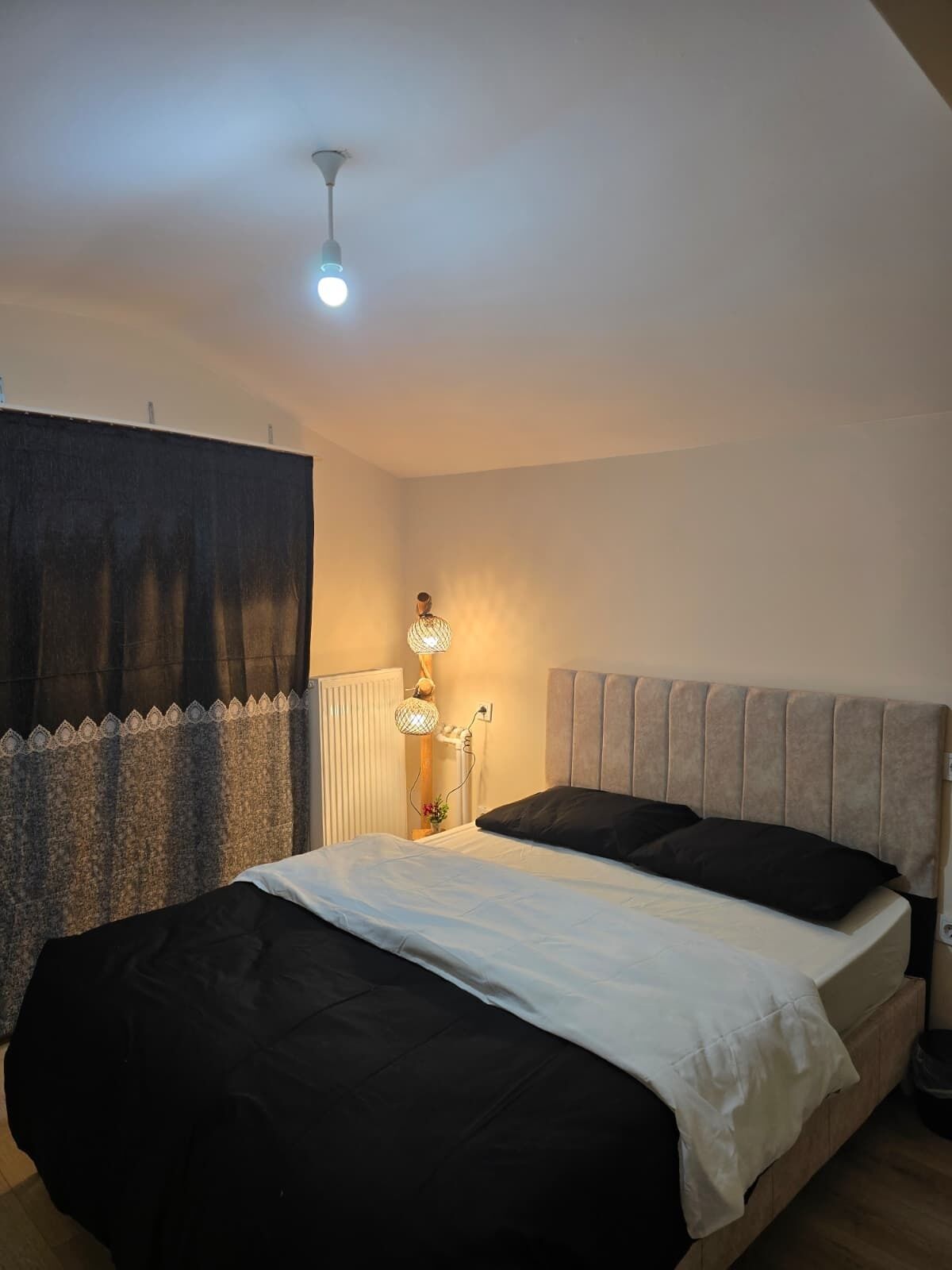 A bedroom with a bed, a bedside table, a lamp, and a radiator.