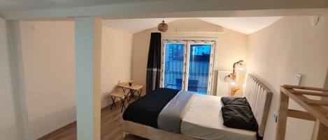 A bedroom with a bed, a small table, a chair, a radiator, and a window with a view.