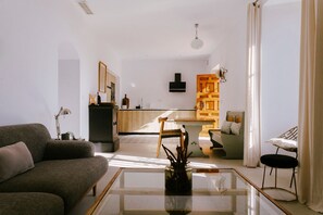 A modern living room with a glass coffee table, a sofa, and a dining area with a chair and table. - Hacienda Clavero: A Garden Apartment (Málaga)
